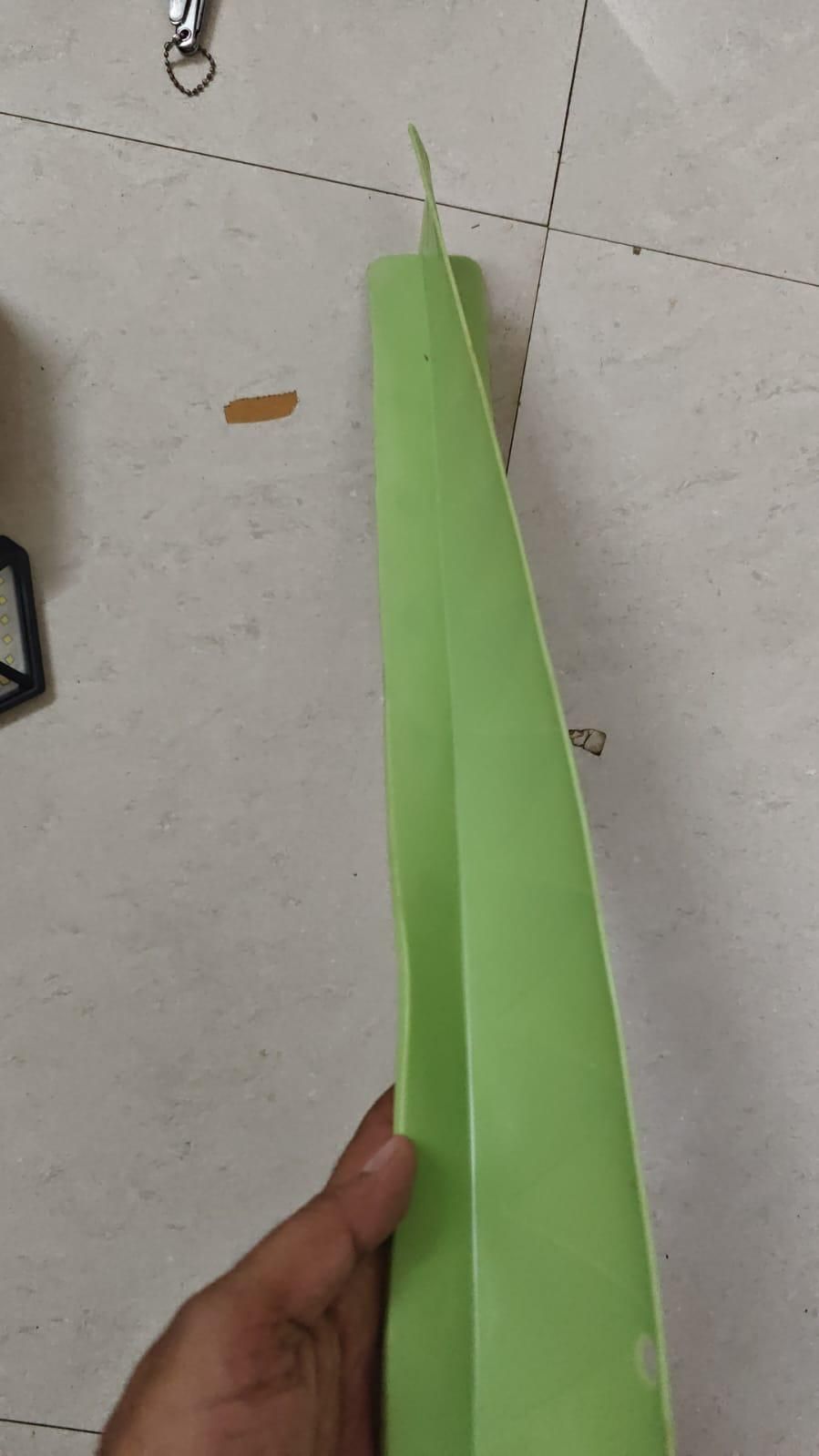 Hand holding a green plastic item, possibly a folder or organizer, on a tiled floor, NayiDeals